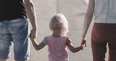 Little girl holding hands of parents.